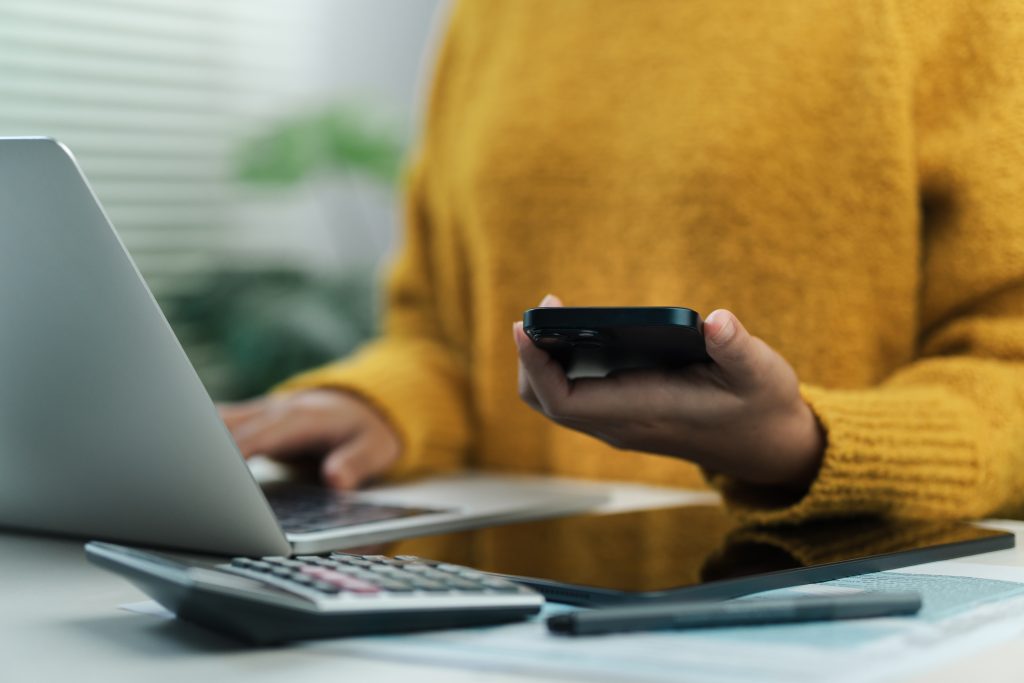 Woman holding calculator and browsing on laptop