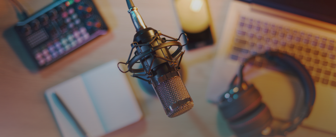 top down image of a studio microphone with a set of headphones, open notebook and a pen