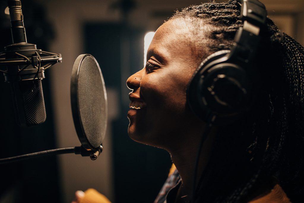 One woman, beautiful black female vocalist wearing headphones and singing into microphone in recording studio.