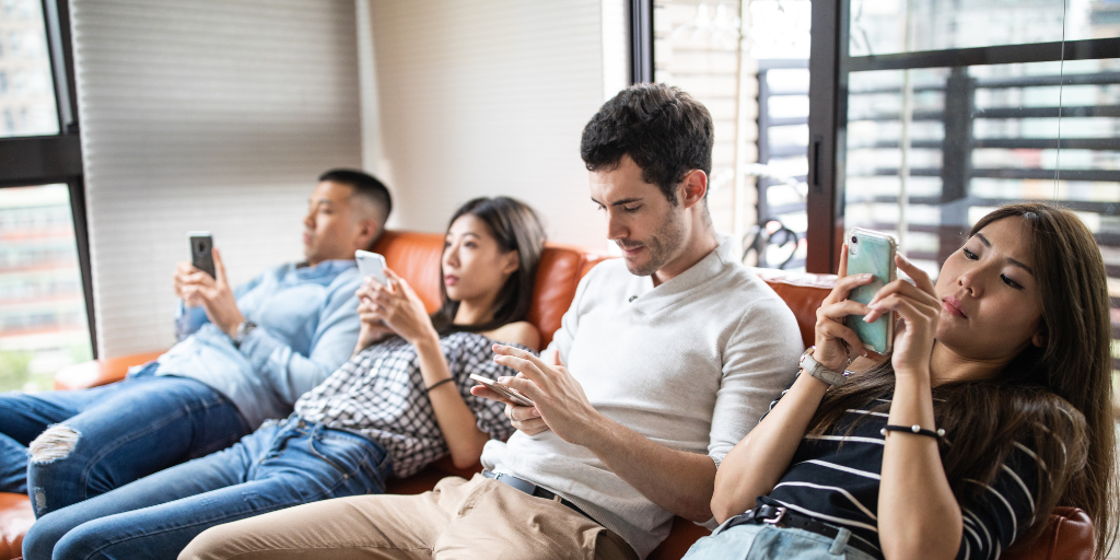 Two men and two women all seated on a couch and looking at their mobile phones