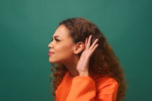 Young biracial woman cups ear, listening intently, green studio background. High quality photo