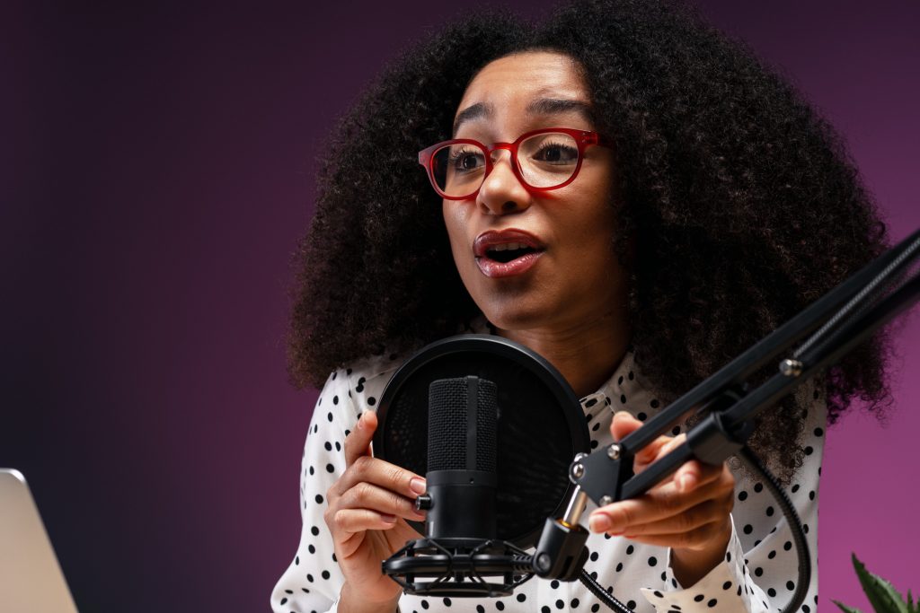 Young woman wearing glasses adjusting her microphone while recording a podcast in professional studio featuring a vibrant purple background, creating engaging audio content. Podcasting concept