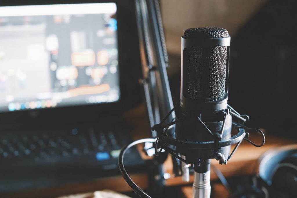 Black condenser microphone on holder arm with anti shake spider, in recording session in front of notebook PC with DAW open, home recording studio