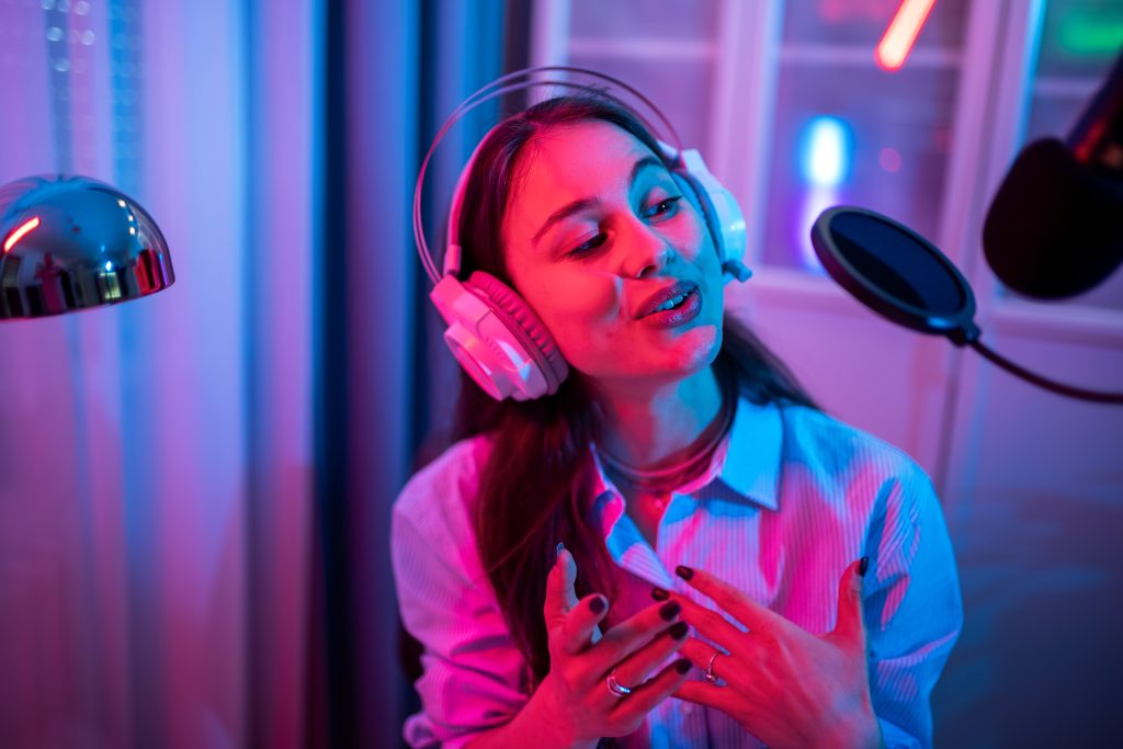 A young woman is recording her own podcast in a modern home studio setup, surrounded by professional equipment.